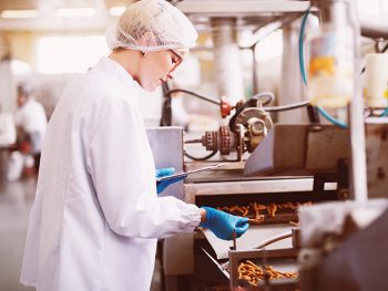 Young female worker in sterile clothes is taking a sample of salt snacks from production line.